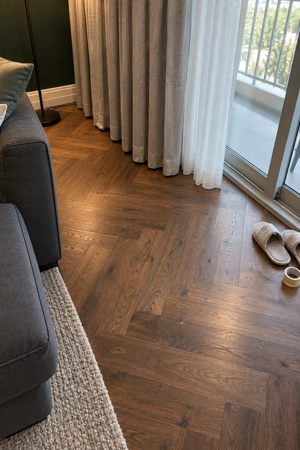 Top-down view of walnut herringbone parquet beside the hem of a pewter linen curtain at a balcony door in The Greens