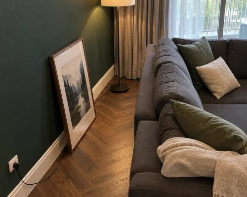 Forest green feature wall meeting white skirting and walnut herringbone parquet in an Al Thayyal 4 apartment